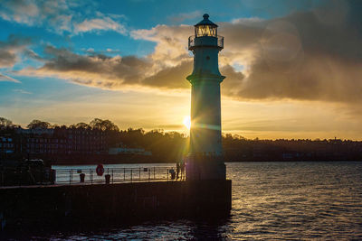 Lighthouse by sea against sky during sunset