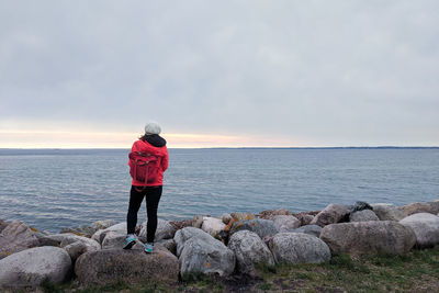 Rear view of man standing on rock by sea against sky