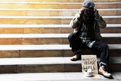 Full length of beggar with message sitting on steps