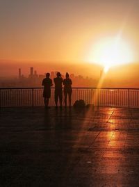 Rear view of silhouette friends standing at observation point against sky during sunset