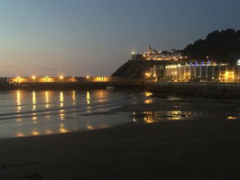 Illuminated city at waterfront during sunset