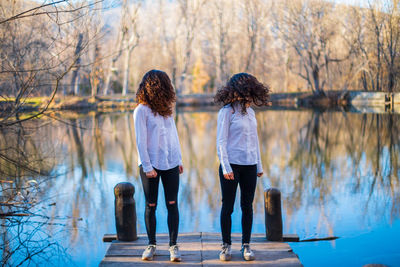 Full length of friends tossing hair while standing on pier by lake in forest