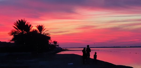 Silhouette people on beach against orange sky