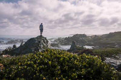 Man standing on rock by sea against sky