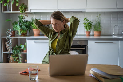 Overworked woman freelancer sitting at table with eyes closed, resting after long hard job on laptop