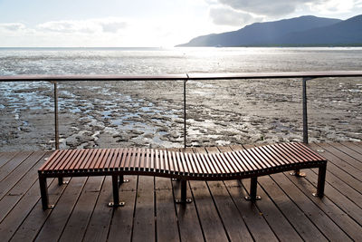 Empty deck chairs by sea against sky