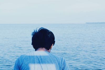 Rear view of man standing by sea against clear sky