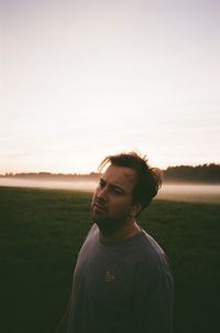 Portrait of young man standing on field against sky