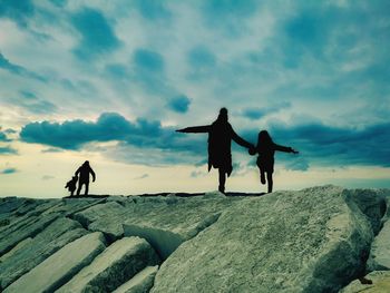 Silhouette men standing on rock against sky