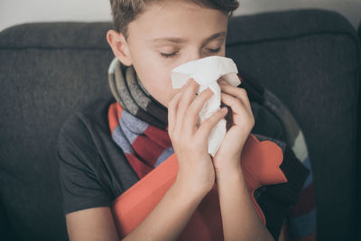 Close-up of boy blowing nose while sitting on sofa