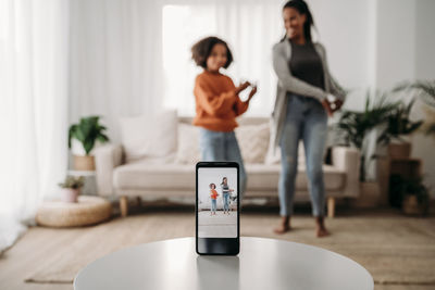 Mother and daughter dancing and filming video through smart phone at home