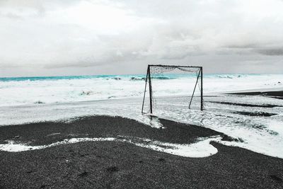 Broken goal post at beach against cloudy sky