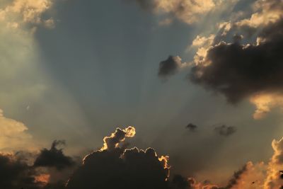 Low angle view of sunlight streaming through clouds during sunset