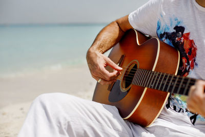 Close-up of a man playing a classical guitar while sitting on the beach in summer. lifestyle.