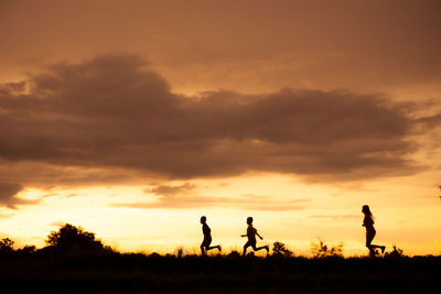 Silhouette people running on field against sky during sunset