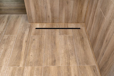 Modern black linear drain in a bathroom lined with ceramic tiles imitating wood.