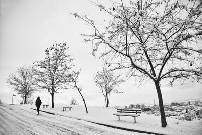 Rear view of man walking on snow covered road against sky