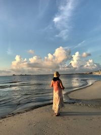Rear view of mature woman walking on beach against sky