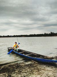 Men sitting on riverbank against sky