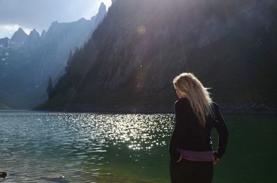 Rear view of woman standing at lakeshore against mountains