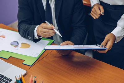 Midsection of business people discussing over document at office