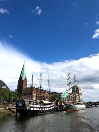 Sailboats moored in river against cloudy sky