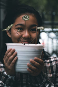 A young girl wearing a plaid shirt holding up a white potted plant in front of her face 