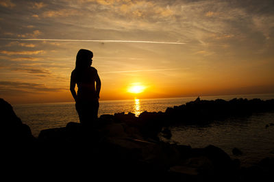 Silhouette man on rock at beach against sky during sunset