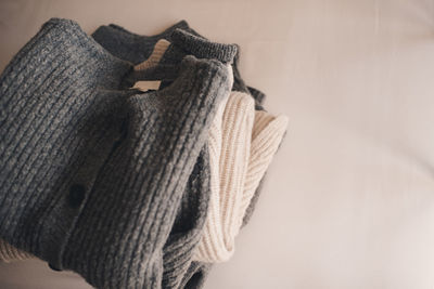 Stack of knitted wool textile sweaters clothes on white blanket in bed at home room close up.