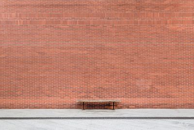 Bench on footpath by brick wall