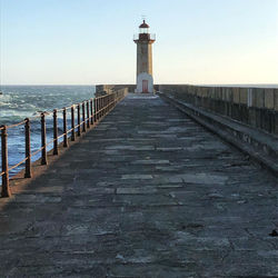 Lighthouse on pier by sea against sky