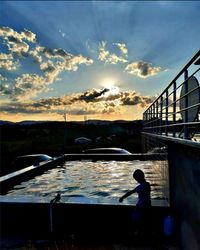 Silhouette man standing by railing against sky during sunset