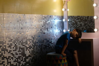 Full length of young man sitting against wall at home