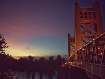 Illuminated bridge over river against sky during sunset