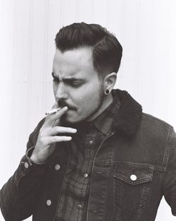 Young man smoking against wall