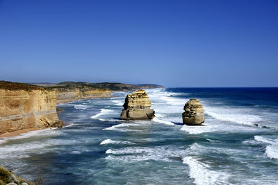 Rocks in sea against clear blue sky