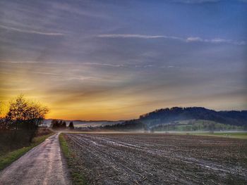 Road amidst field against sky during sunset