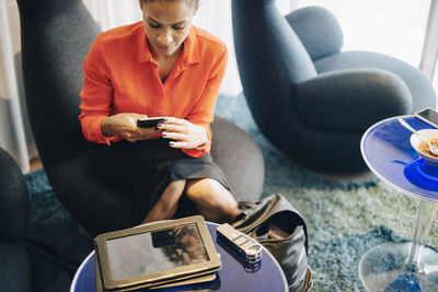 High angle view of businesswoman using smart phone while sitting on chair at office cafeteria