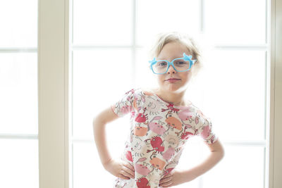 Portrait of girl wearing eyeglasses standing by window at home