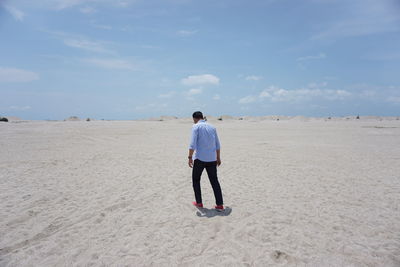 Rear view of man standing on beach against sky