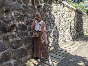 Full length of woman standing against wall outdoors