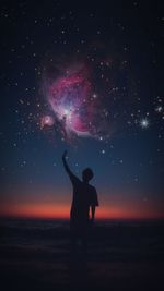 Rear view of silhouette man standing in sea against sky at night