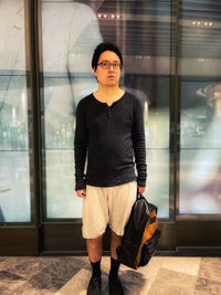 Portrait of young asian man in eyeglasses standing in front of illuminated reflective panels.