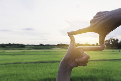 Midsection of person holding umbrella on field against sky