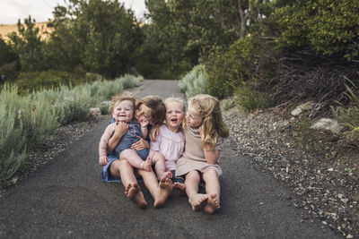 Happy cute sisters sitting on road in forest