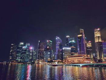 Illuminated buildings by river against sky at night