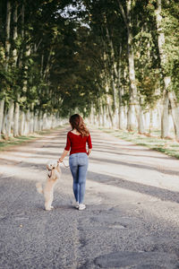 Rear view of woman walking with dog on footpath