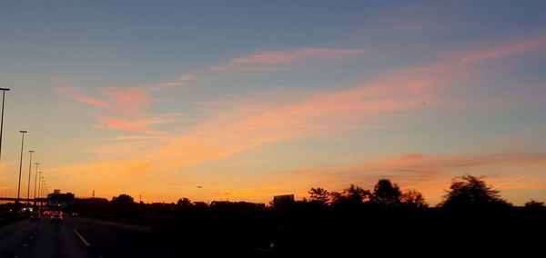 Silhouette trees by road against sky during sunset