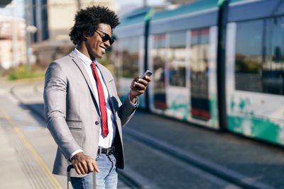 Young man using mobile phone while standing at railroad station