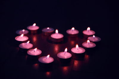 Close-up of illuminated tea lights decorated in heart shape on table at darkroom